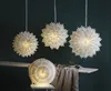 Four paper star lanterns are displayed in a dimly lit room. Three are hanging from the ceiling, and one is placed on a chair. Podgląd zdjęcia produktu
