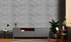 A modern living room with a grey TV console against a textured grey brick wall, decorated with plants and a lamp. Náhľad obrázku produktu