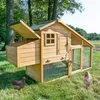 A wooden chicken coop with an attached run is set up on a grassy lawn, with two chickens nearby. Trees and a field are visible in the background. Produktbild-Vorschau
