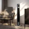 A tall, slim tower fan is positioned next to an armchair in a room with soft lighting and shadows. Podgląd zdjęcia produktu