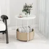 A small round white side table with a storage basket underneath, holding books. A cup of tea and macarons are on the table, along with a vase of flowers. A chair is partially visible on the left. Anteprima dell’immagine prodotto
