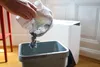 A hand is pouring the contents of a white bag into a gray bin. Produktbild-Vorschau
