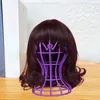 A brown wig is displayed on a purple wig stand, placed on a wooden surface. In the background, there is a white textured wall and a white book. Produktbild-Vorschau