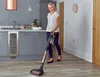 A woman is vacuuming a kitchen floor with a cordless vacuum cleaner. Produktbild-Vorschau