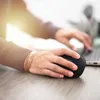 A person's hands using a black wireless mouse on a wooden desk, with a laptop in the background. Produktbild-Vorschau