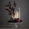 A white cake stand with LED candles, a pomegranate, moss, and decorative branches. Produktbild-Vorschau