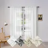 A room scene with white sheer curtains hanging over a window, a chair and a lamp to the left, and fabric swatches at the bottom. Produktbild-Vorschau