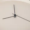 A close-up view of the hands of a clock on a plain, light-colored background. Anteprima dell’immagine prodotto