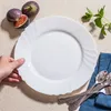 A hand holding a white plate with figs and mint in the background. Anteprima dell’immagine prodotto