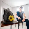 A young man is tying his shoes in a locker room, with a backpack containing a soccer ball next to him. Produktbild-Vorschau