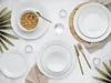 A top-down view of a table setting with white porcelain plates, bowls, cutlery, and decorative elements. Produktbild-Vorschau