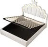 A white bed frame with the mattress support lifted to reveal storage space underneath. The headboard is shaped like a crown with LED lighting. Náhled obrázku produktu