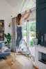A woman is cleaning the top of a window frame while standing on a ladder in a well-lit room. Anteprima dell’immagine prodotto