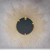 The back of a sunburst mirror is shown against a textured gray wall. Produktbild-Vorschau