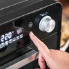 A close-up shot of a person's finger pressing a button on the control panel of a black mini-oven. Anteprima dell’immagine prodotto