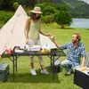 A couple is camping by a lake, with a tent and a portable table set up for a meal. Produktbild-Vorschau