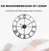 A large metal wall clock with Roman numerals is shown against a white background, with a blurred image of a person sleeping in the foreground. Produktbild-Vorschau