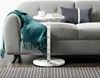 A marble-look C-shaped side table with a teal throw blanket draped over a gray sofa. Produktbild-Vorschau