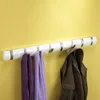 A white flip-hook coat rack mounted on a yellow wall, with two scarves and a coat hanging on it. Podgląd zdjęcia produktu