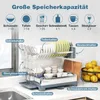 A two-tier dish drying rack with various kitchenware items, including plates, glasses, bowls, and cutlery, displayed on a kitchen countertop next to a sink. The image also features lemons in a basket and cutting boards. Podgląd zdjęcia produktu