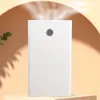 A white humidifier with a power button is placed on a light brown surface, with a plant and shadows in the background. Produktbild-Vorschau