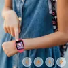 A child's hand is shown interacting with a pink smartwatch on their wrist. Produktbild-Vorschau