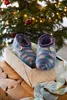 A pair of knitted slippers in a gift box, with a Christmas tree in the background. Produktbild-Vorschau