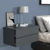 A modern gray floating nightstand with two drawers is mounted on a blue wall next to a bed with white pillows. A framed picture of a deer on a cliff and a white table lamp are on top of the nightstand. Produktbild-Vorschau