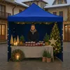 A woman stands behind a market stall decorated for Christmas, selling jars of preserves. Produktbild-Vorschau