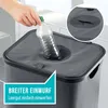 A hand is shown inserting a plastic bottle into a gray laundry hamper with a wide opening. Podgląd zdjęcia produktu