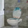 A toilet with a lid and seat decorated with a beach and ocean wave pattern, situated in a bathroom with marble-tiled walls. Produktbild-Vorschau