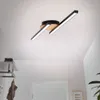 A modern ceiling light fixture with black and wood accents is mounted on a white ceiling in a hallway. Produktbild-Vorschau