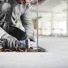 A person is using an angle grinder to cut a metal rod on a concrete surface. Produktbild-Vorschau