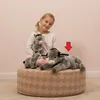A young girl is sitting on a round ottoman with three stuffed donkeys. Anteprima dell’immagine prodotto