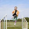 A young girl is jumping over a hurdle while holding a black stuffed horse toy. Anteprima dell’immagine prodotto