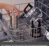 A hand places a metal filter into a dishwasher rack next to a glass teapot. Produktbild-Vorschau
