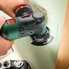 A person is using a green and black oscillating multi-tool to cut into a light green wall. Voir les images du produit