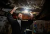 A mechanic is inspecting the underside of a car with a flashlight in a workshop. Produktbild-Vorschau