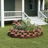 A garden bed border made of metal with a rust-like finish, surrounding a variety of flowering plants in front of a house with a porch and steps. Produktbild-Vorschau