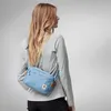 A woman wearing a grey long-sleeved shirt and black pants is shown from the back, wearing a light blue crossbody bag. The background is a plain light grey. Anteprima dell’immagine prodotto