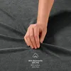 A hand is shown touching a dark gray fabric, likely a bedsheet, with text and a cotton icon overlaid. Anteprima dell’immagine prodotto