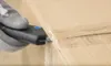A gloved hand is using a utility knife to cut through the plastic wrap on a cardboard box. Voir les images du produit