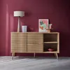 A wooden sideboard with slatted doors is displayed against a deep red wall, with a lamp, artwork, and decorative items on top. Anteprima dell’immagine prodotto