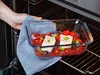 A hand is placing a glass baking dish filled with food into an oven. Anteprima dell’immagine prodotto