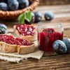 A rustic scene with slices of bread spread with plum jam, a jar of jam, and fresh plums on a wooden table. Voir les images du produit