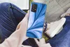 A person holding a smartphone with a blue abstract design case while sitting down. Produktbild-Vorschau