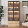 A tall, narrow cabinet with glass doors and wooden drawers, filled with decorative items and books, set against a wall with decorative molding. Voir les images du produit