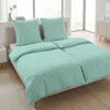 A neatly made bed with mint and white striped bedding, two pillows, and a duvet, in a bright room with large windows. Produktbild-Vorschau