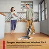 A couple is in a modern kitchen. The man is using a wet-dry vacuum cleaner to clean up a spill on the floor, while the woman holds a plate with a pastry. Produktbild-Vorschau