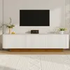 A white TV console with a fluted front and a gold base, placed in a modern living room setting with a large black TV mounted on the wall above it. A rug with a geometric pattern is on the floor in front of the console. Anteprima dell’immagine prodotto